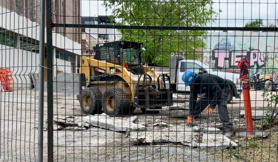 On voit un homme déplaçant des blocs en béton, derrière un grillage et tout au fond une murale couverte des lettres TER.