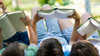 La photo montre trois enfants couchés sur le dos à l'extérieur, un livre devant eux.