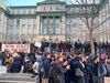 On voit des manifestants regroupés aux alentours du trottoir devant le bâtiment patrimonial de la rue University.