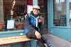 M. Gao pose assis sur la banquette devant le restaurant Les Belle-Sœurs.