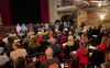 Une salle avec des chaises et des dizaines de personnes assises, face à neuf candidats et une présentatrice.