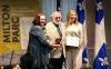 Les trois personnes sont debout sur une petit scène et tiennent une médaille et un certificat.