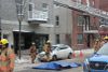 On voit, de jour, huit pompiers devant l'extérieur du restaurant et l'échelle du camion de pompier dirigée vers le toit de l'immeuble.