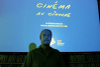 M. Meech pose devant l'écran bleu où l'on peut lire «Cinéma au cinoche». Derrière lui se trouvent des étagères pleines de DVD.