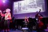Brigitte Therrien prend le micro devant trois musiciens d'Et plusieurs autres ainsi qu'une projection de photo d'époque d'une rue commerciale du Plateau.