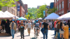 Vue dirigée vers le mont Royal: une foule piétonne se promène entre les kiosques d'une foire commerciale. 