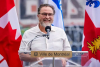 M. Ryan sourit, debout derrière un podium et devant des drapeaux du Canada, du Québec et de Montréal.