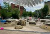 Des enfants jouent parmi les roches et les jets de bruine de la place des Fleurs-de-Macadam.