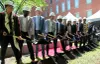 Onze personnes avec des casques de construction tiennent une pelle remplie de terre, devant un tapis rouge, sous le soleil de printemps.