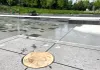 Un rond en bois est posé sur un trou dans une surface en pierre, près de jeux d'eau.