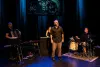 M. Sioui se tient debout, en plein conte, devant trois musiciens.