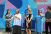 Mme Belley parle dans un microphone, avec cinq élus du Plateau autour d'elle. Sa murale est dominée par des teintes de bleu, vert et rose. 