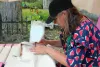 Vêtue d'habits à motifs de melon d'eau, Mme Van Roost. est concentrée sur ce qu'elle brode à l'aide de sa machine à coudre.