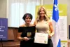 Les deux femmes posent avec une médaille et un certificat, devant un drapeau du Québec.