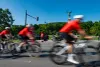 Des cyclistes floutés semblent passer à toute vitesse sur l'avenue du Parc, devant le mont Royal, un policier à moto et la mascotte des Championnats du monde UCI.