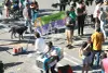 Plusieurs personnes sont éparpillées sur le pavé de l'avenue du Parc. L'une d'entre elle est vêtue d'un déguisement d'autobus 80 du Parc. On voit aussi un filet de jeu de parc et une bannière