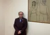 Adrien Welsh pose près d'un tableau où une femme et un homme, habillés simplement, se tiennent une main levée.