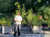 Le candidat, un jeune homme, se tient debout devant des bacs de plantation, avec une chemise blanche à manches courtes 