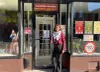 La candidate se tient devant un local commercial avec une affiche "Quartier Général Marxiste-Léniniste"
