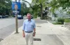 Philippe Schnobb pose sur un trottoir, près d'une pancarte électorale qui le représentan.