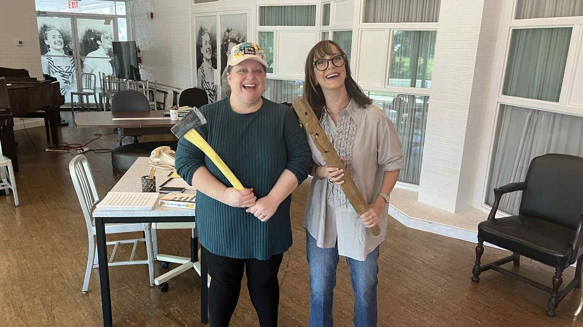 Two women laugh while holding prop weapons during rehearsal inside a bright studio at freeFall Theatre in St. Petersburg, Florida.