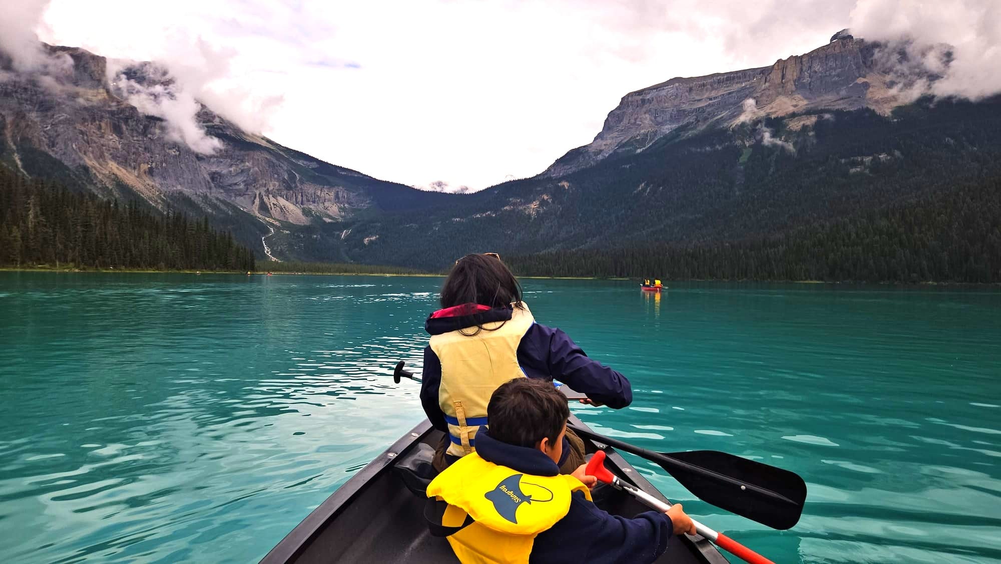 Mother and child paddling kayak on Emerald Lake Yoho National Park backs to camera turquoise water mountains