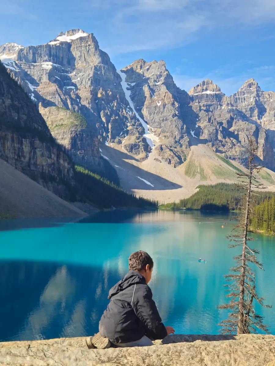 Young child in rain coat back to camera looking at Moraine Lake sunrise Banff National Park Canadian Rockies