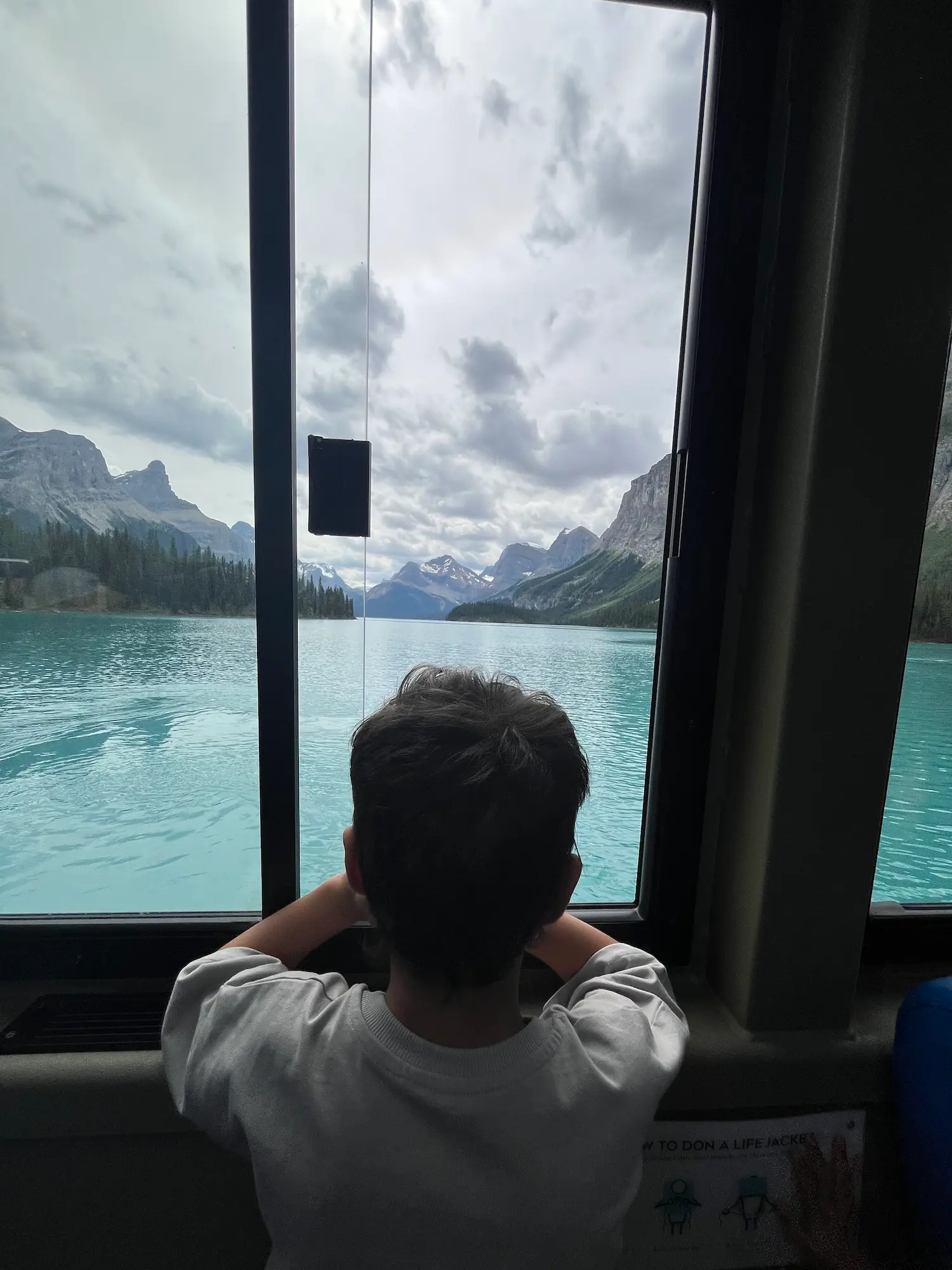 Child's back to camera looking through the window of the covered cruise boat at Spirit Island on Maligne Lake, Jasper National Park