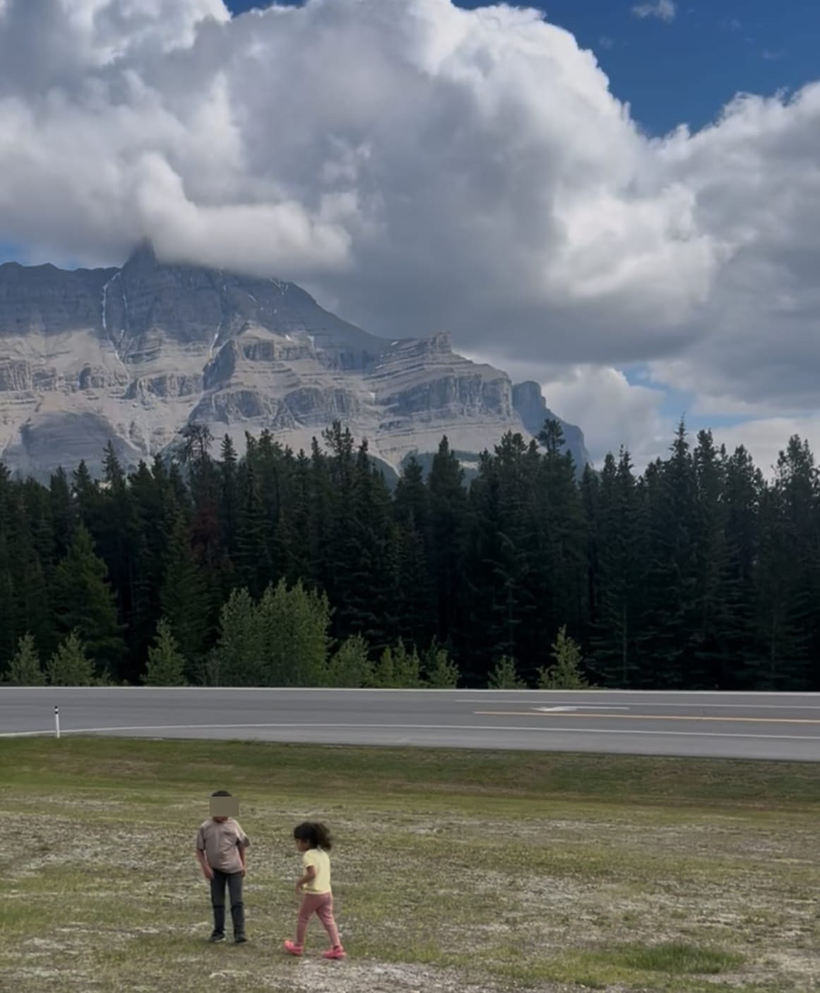 Two young children walking on grass with Mount Rundle rising behind them at a roadside stop on the Icefields Parkway, Banff National Park