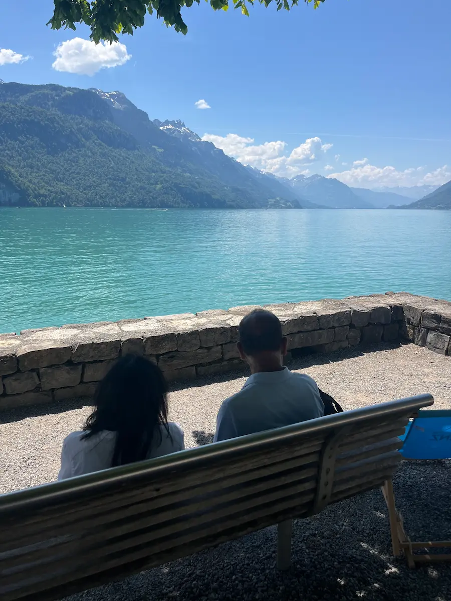 Grandparents sitting on bench at Lake Brienz shoreline facing turquoise alpine water, Bernese Oberland