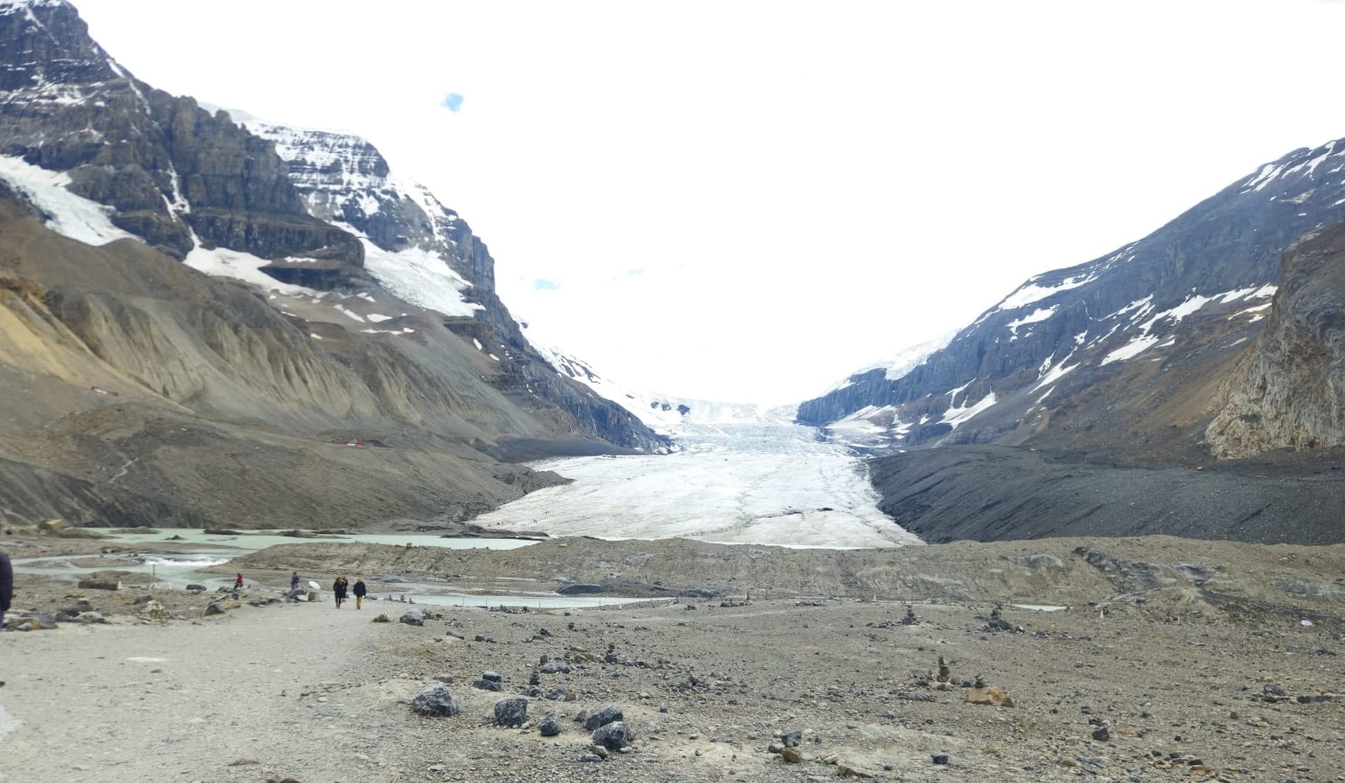 Distant figures walking the gravel moraine path toward the Athabasca Glacier toe at the Columbia Icefield, Jasper National Park, Canada