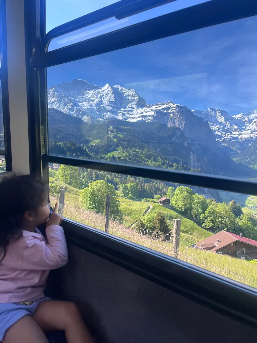 Child back to camera at train window pointing at snow-capped Swiss Alps mountains, Jungfrau Region Switzerland family train travel