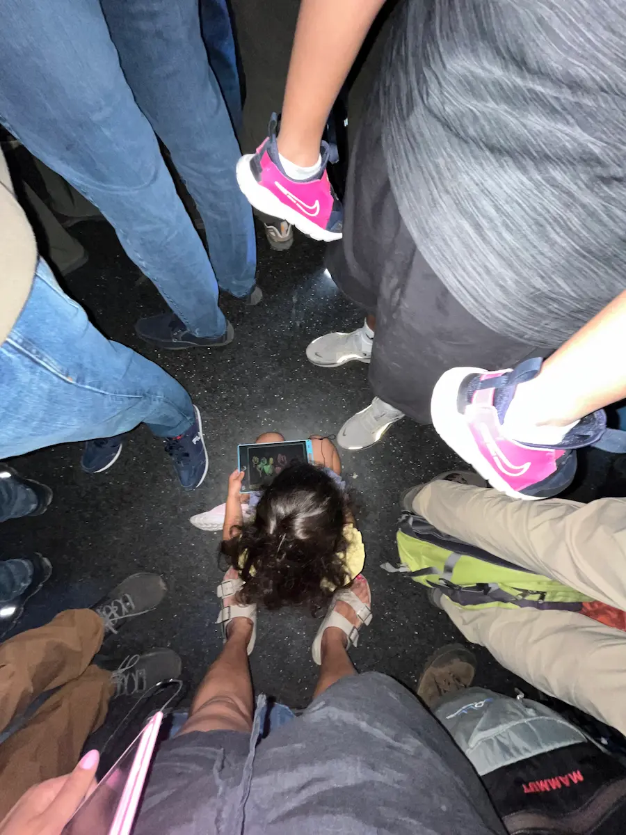 Toddler sitting on floor of crowded cable car playing with tablet surrounded by family feet, Jungfrau Region Switzerland travel with toddlers