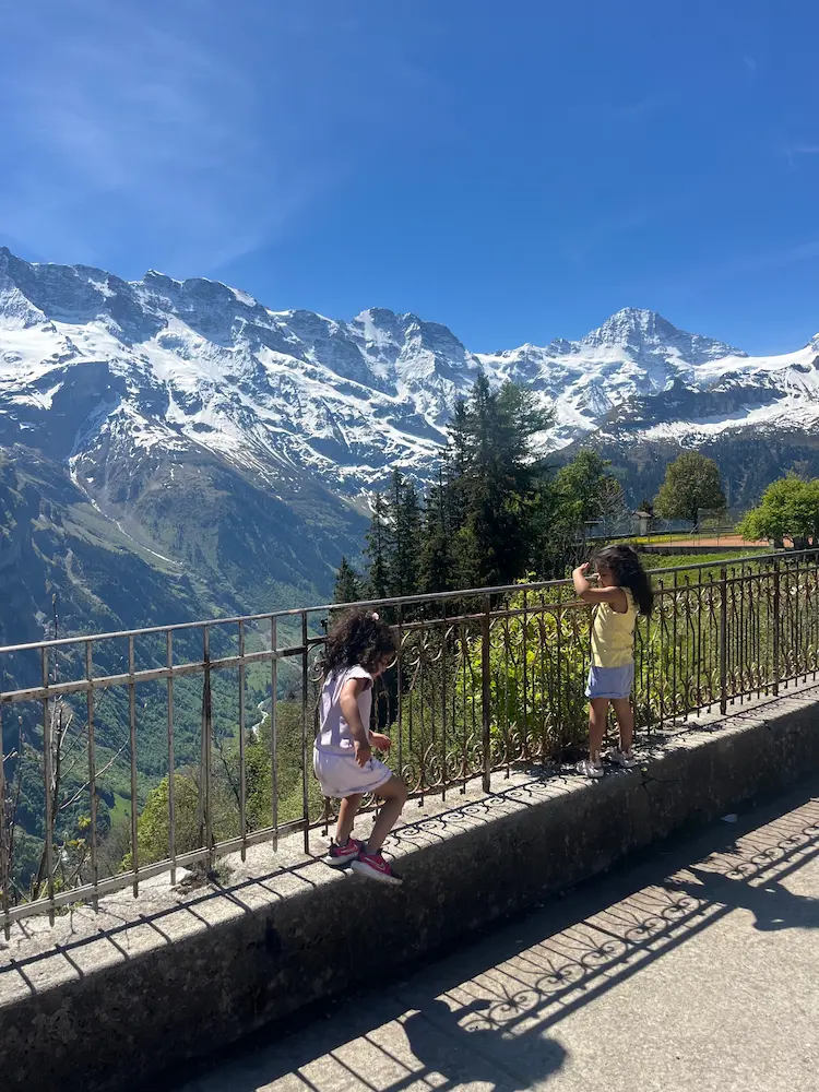 Family walking mountain path backs to camera with Eiger and snow-capped peaks behind, Mürren to Gimmelwald walk Switzerland