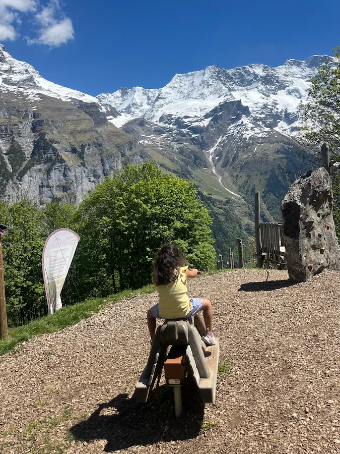 Child on playground with Eiger and snow-capped peaks behind, Gimmelwald Jungfrau region Switzerland