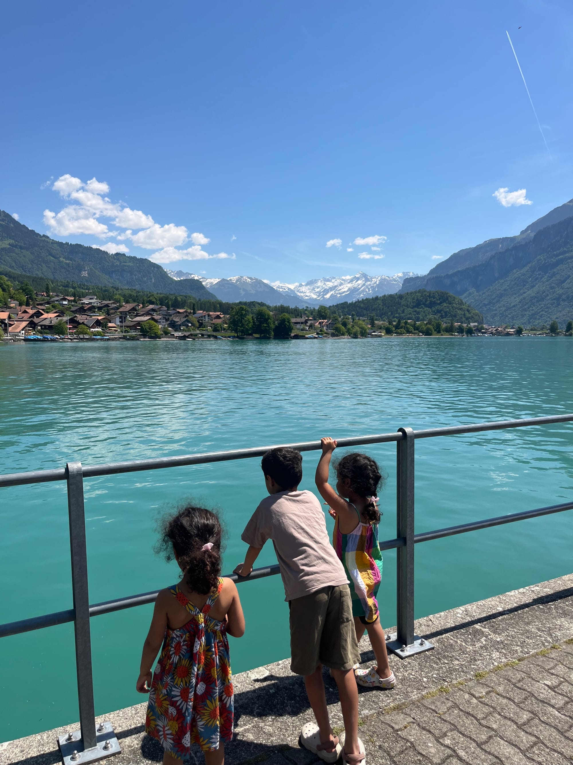 Children at waterfront quayside backs to camera, turquoise Lake Brienz and Swiss Alps behind, Jungfrau region