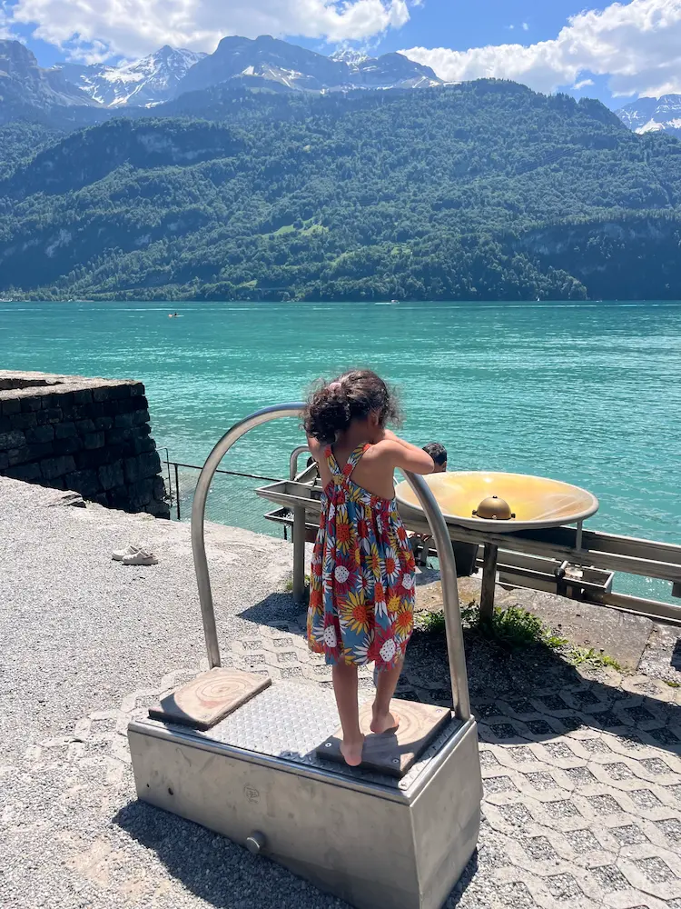 Child standing on bollard at Lake Brienz waterfront, turquoise water and Swiss Alps behind, Brienz Switzerland