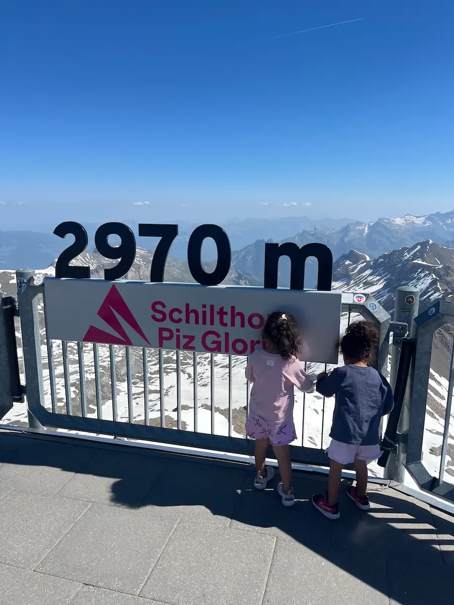 Family at Schilthorn summit altitude sign at 2970 metres with snow-capped Alpine panorama, Piz Gloria Jungfrau region