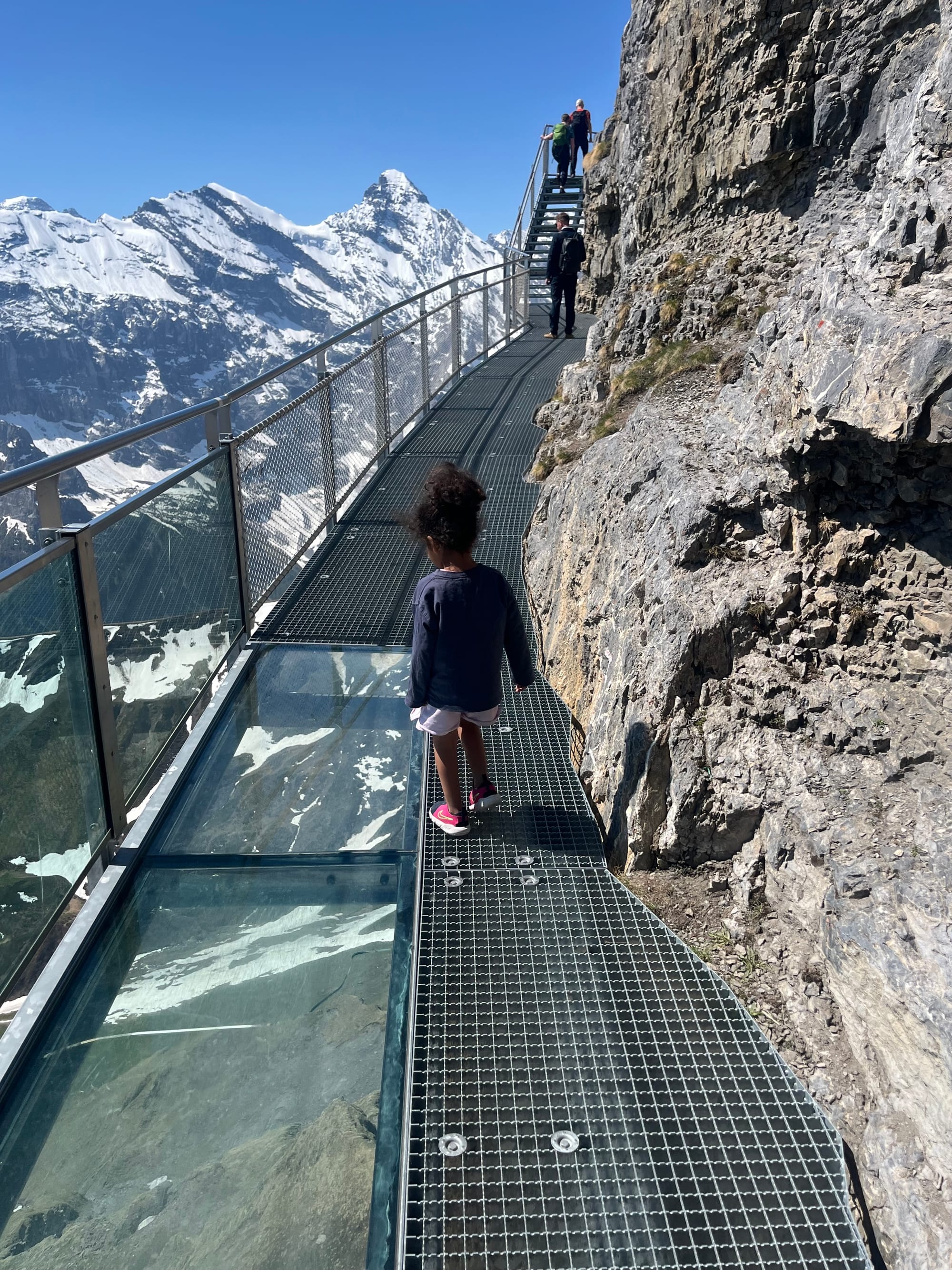 Person back to camera on Birg Thrill Walk glass walkway, open Alpine drop below, Schilthorn Jungfrau region Switzerland