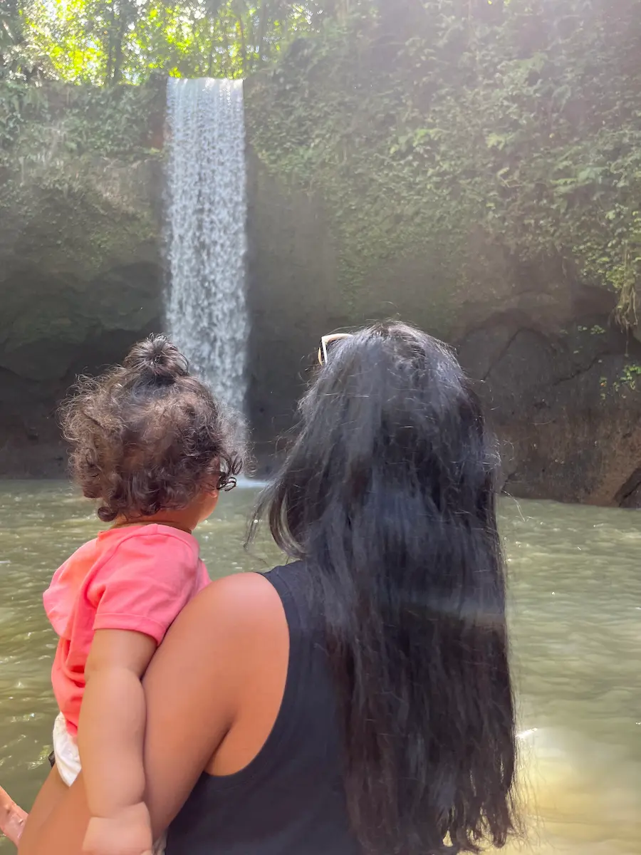 Tibumana Waterfall in lush Bali jungle with a small distant figure showing scale of the descent