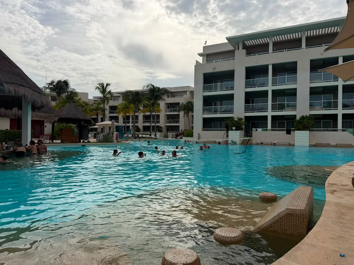 Wide view of a resort pool with swimmers at a distance, Paradisus Playa del Carmen, palm trees surrounding