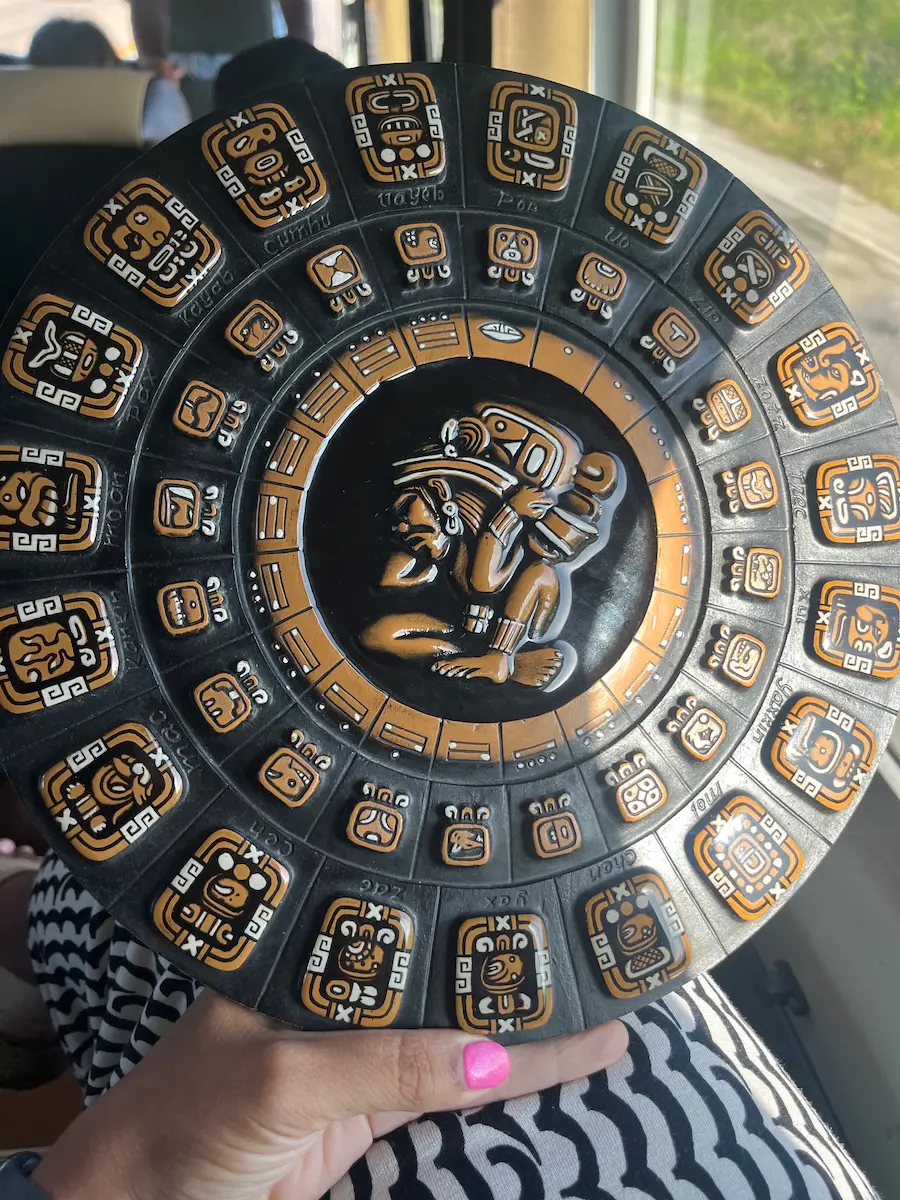 Circular carved Mayan calendar held up on the tour bus, intricate glyphs and central figure detail visible.