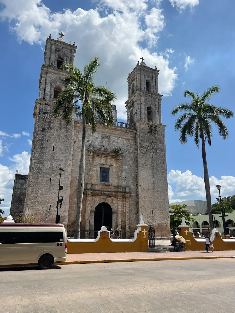 Colonial-era church facade in Valladolid, twin bell towers against a blue sky, palm trees framing the entrance.