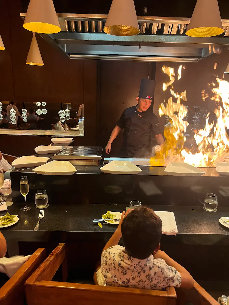 Chef cooking teppanyaki-style with visible flames at Bana Family restaurant, Paradisus Playa del Carmen.
