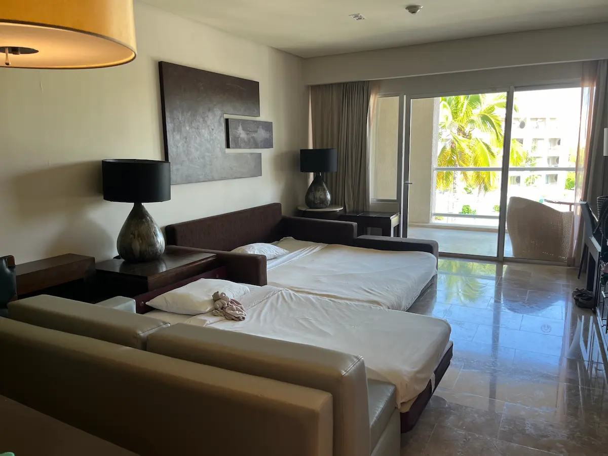 Pull-out sofa bed made up with pillows in a Master Suite living room at Paradisus Playa del Carmen, balcony doors open beyond.