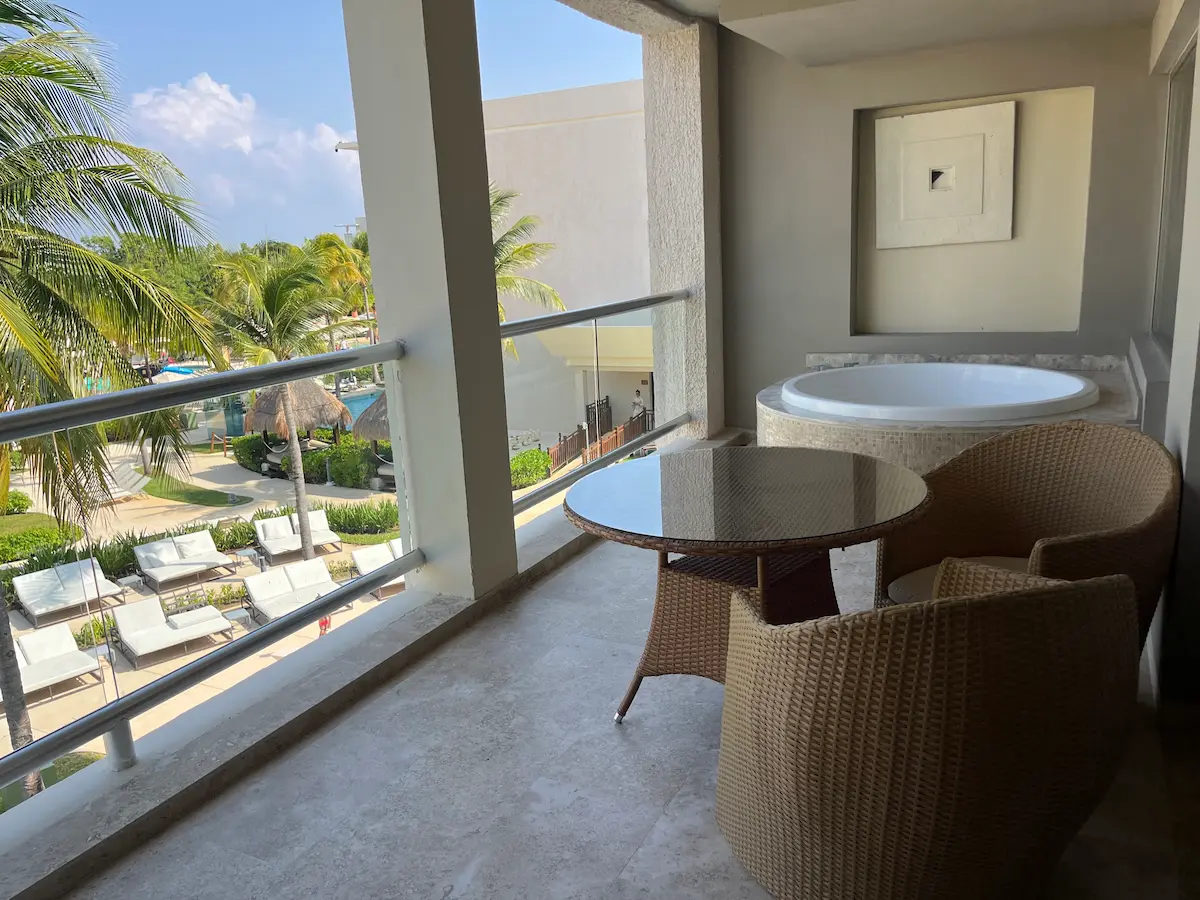 Balcony jacuzzi tub and wicker seating overlooking the pool at Paradisus Playa del Carmen, palm trees framing the view.