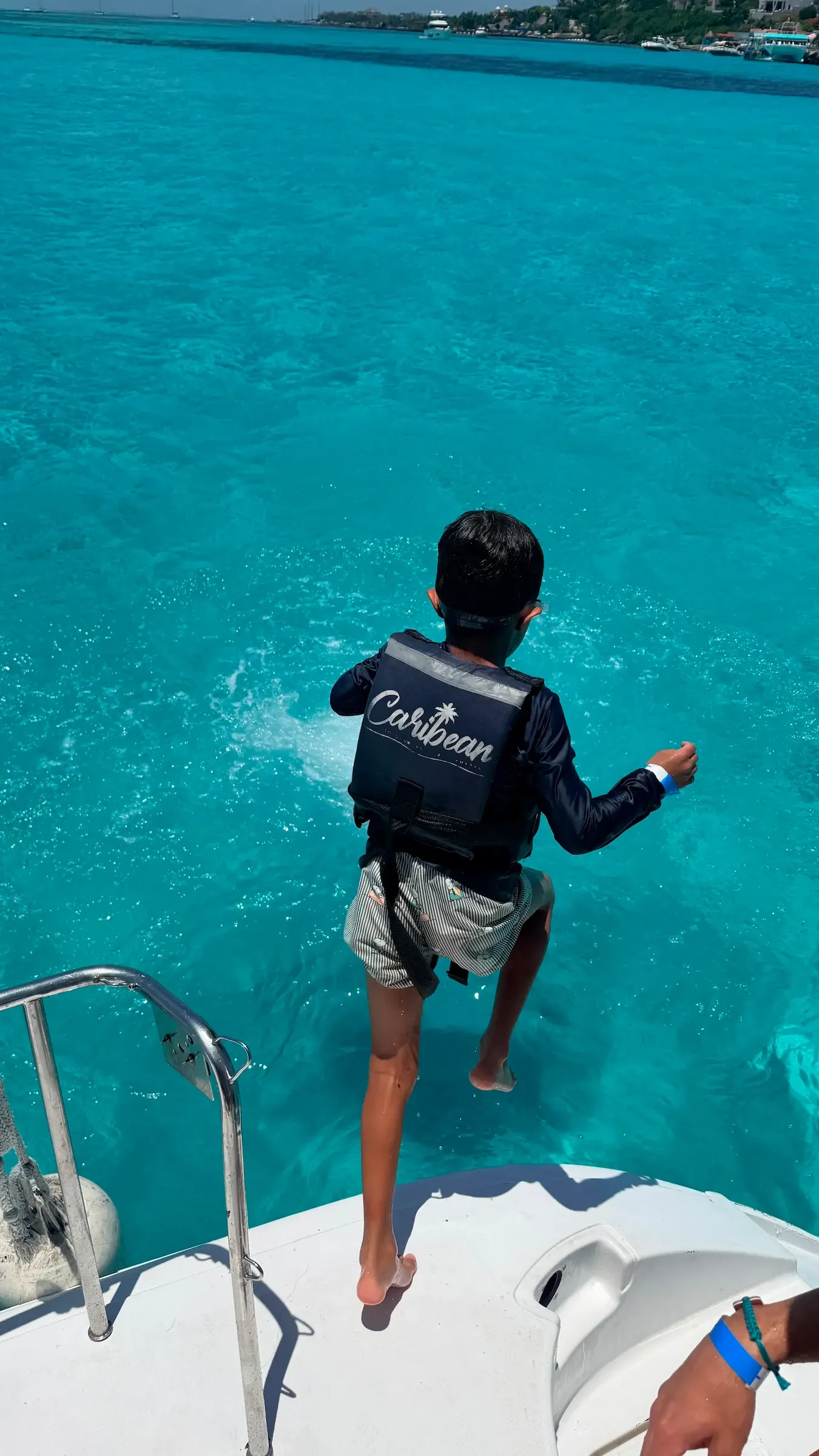Child in a life vest jumping off the bow of a catamaran into turquoise water, mid-air, splash below.