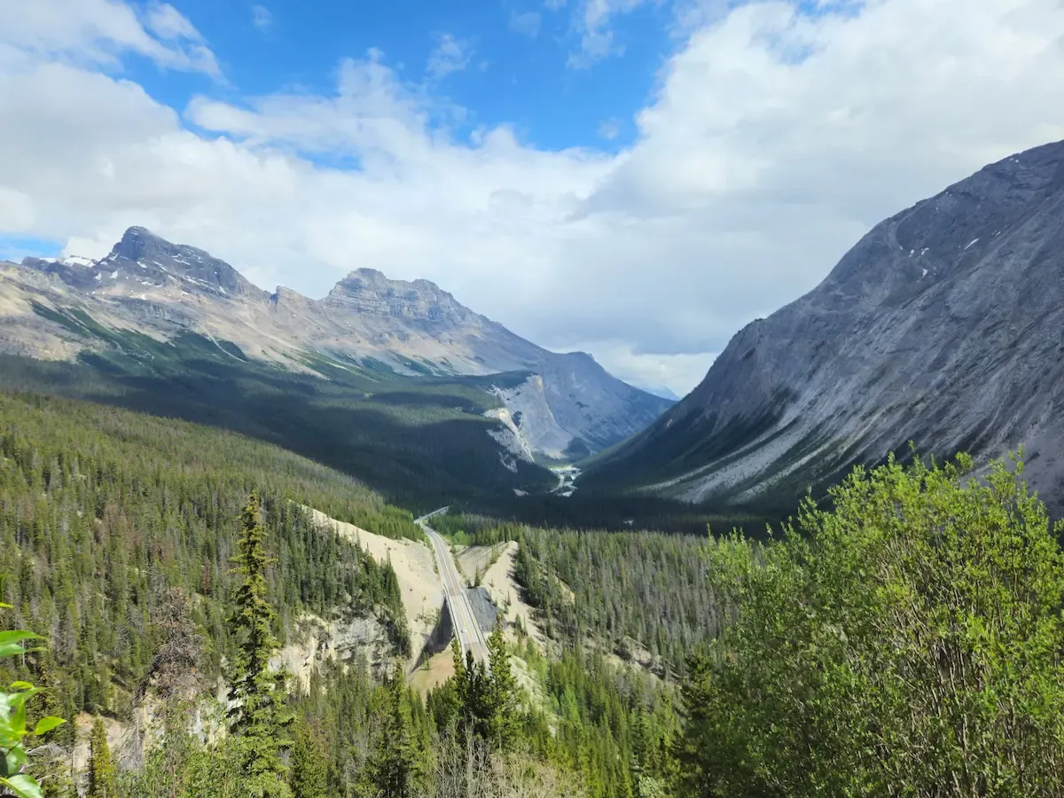 Aerial view of the Icefields Parkway road winding through a forested valley with mountains rising on both sides, Banff National Park, Canada