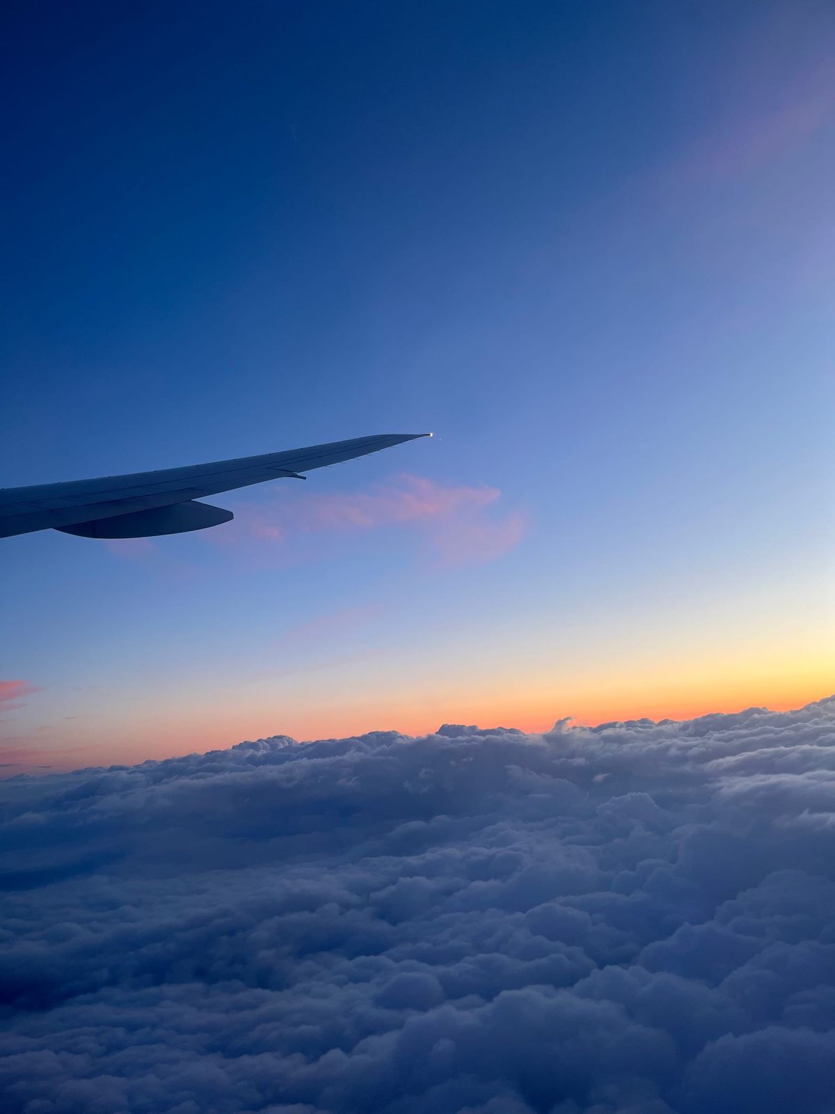 Aeroplane wing silhouetted against a sunset above clouds, en route to Mauritius for a multi-generational family destination wedding.