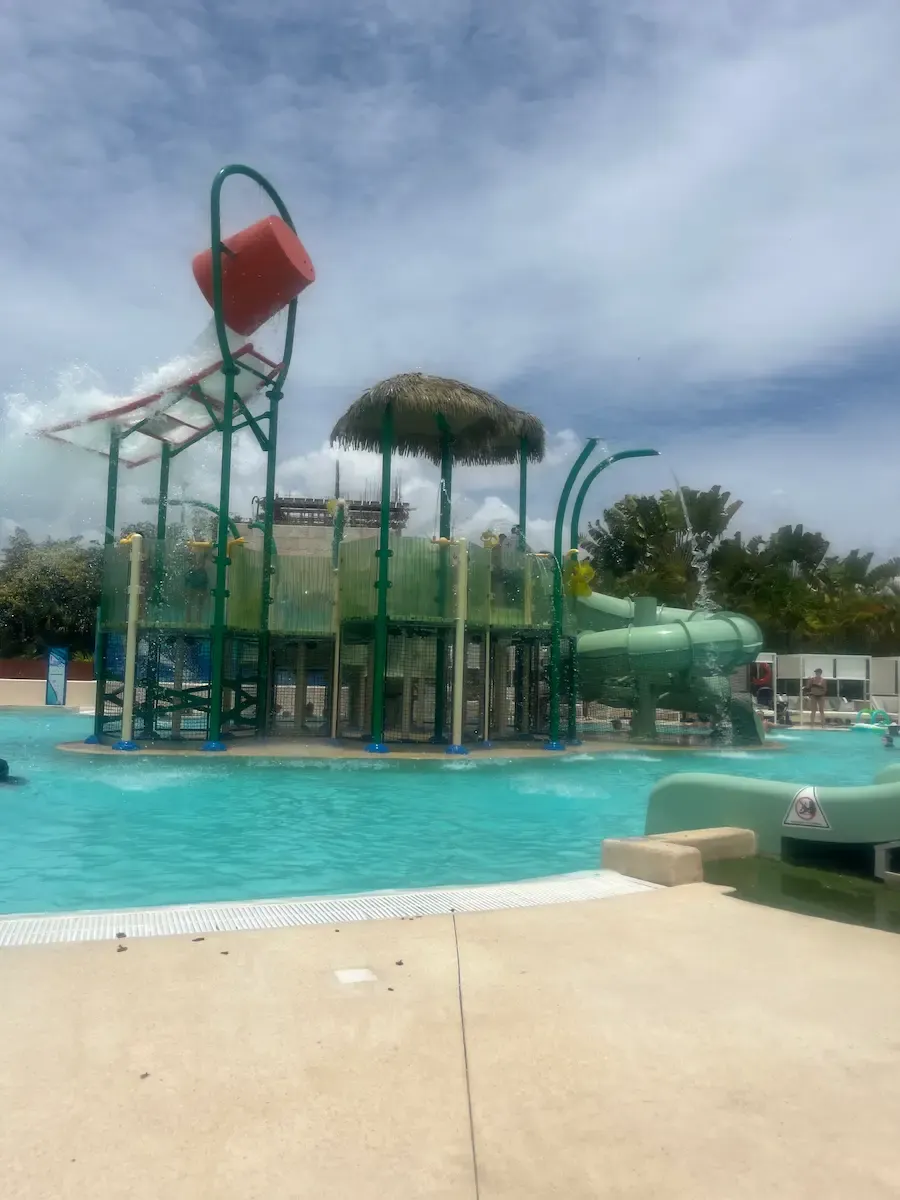 Main pool at the Paradisus Playa del Carmen aqua park, slides and loungers visible, palm trees surrounding.